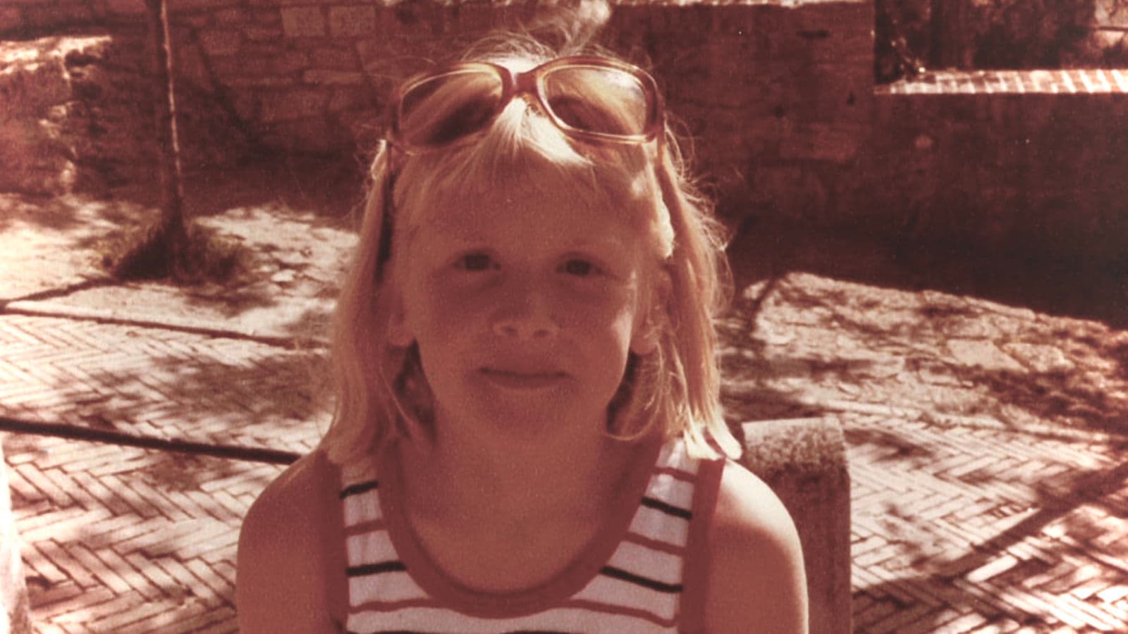Caroline as a child, sunglasses pushed up on her head, on a sunny day.