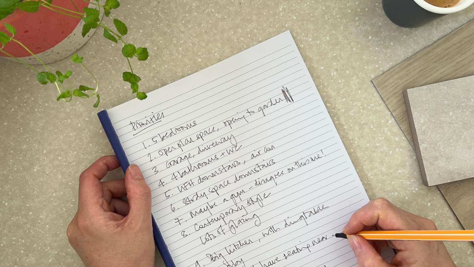 Handwritten list of priorities for a build project on a pad of paper, with a hand holding a pen